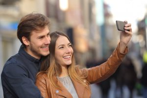 Couple taking selfie photo with a smart phone in the street with an unfocused background